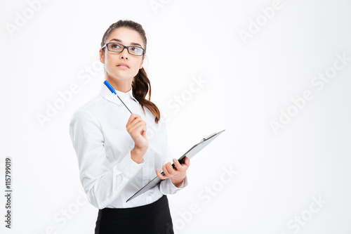 Pensive young businesswoman with clipboard holding pen