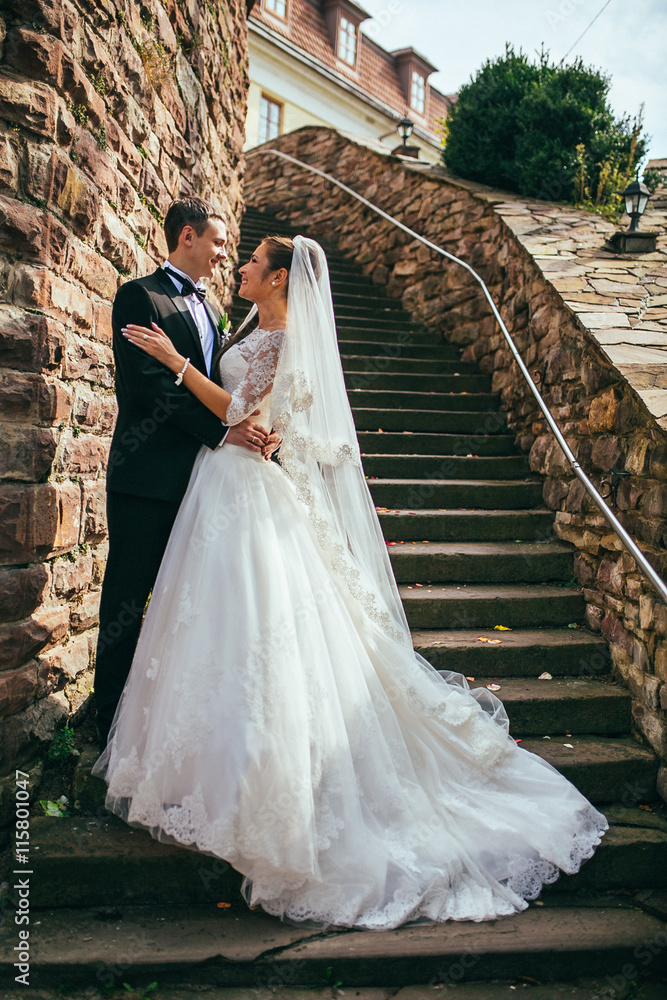 Romantic valentyne couple, bride and groom posing at old stairs and stone wall. Newlyweds  embracing and kissing.