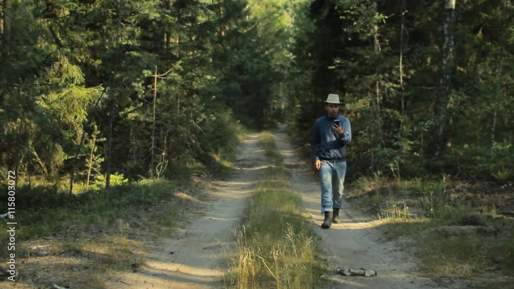 A man walks through the forest with the phone and looks at the navigation application. He chooses the right direction A man walks through the forest with the phone and looks at the navigation application. He chooses the right direction