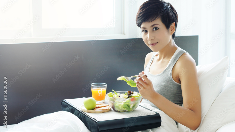 Asian woman having light breakfast fruit salad juice in bed