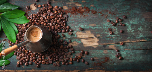 Hot coffee in a coffeepot or turk on a wooden background with coffee leaves and beans, horizontal with copy space. Top view