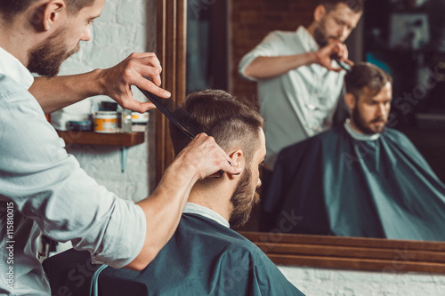 Young handsome barber making haircut of attractive man in barbershop photo