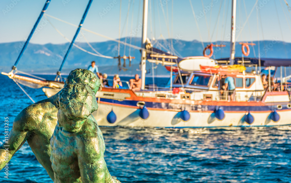 Obraz premium Daily trip on Island of Brac / .Sculpture of fisherman in foreground with touristic boat in background in Island of Brac, Bol town, Croatia.