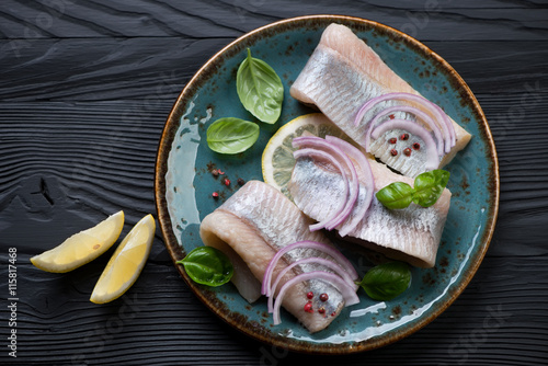 Fotografie Plate with herring fillet on a black wooden background, top view