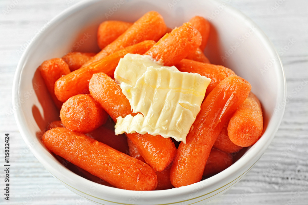 Cooked baby carrots with butter piece in white soup plate, close up Cooked baby carrots with butter piece in white soup plate, close up
