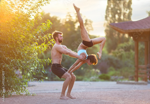 Acro yoga  two sporty people practice yoga in pair  couple doing stretching exercise in the garden with evening sunset on background