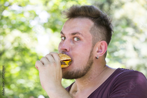 emotional young guy eating a cheeseburger on the nature