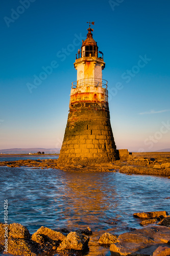 Plover Scar lighthouse at Cockerham on Morecambe Bay in the UK. The lighthouse has been damaged by the sea. At sunset.