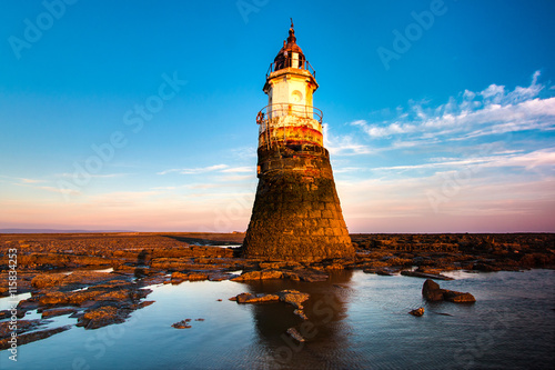 Plover Scar lighthouse at Cockerham on Morecambe Bay in the UK. The lighthouse has been damaged by the sea. At sunset.