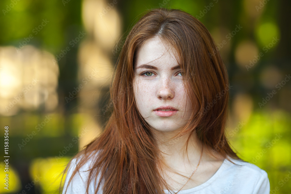 Portrait of a young redhead woman staring into the camera outdoor blurry forest park background Portrait of a young redhead woman staring into the camera outdoor blurry forest park background
