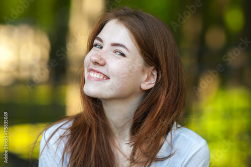 Portrait of a young redhead woman smiling into the camera outdoor blurry forest park background