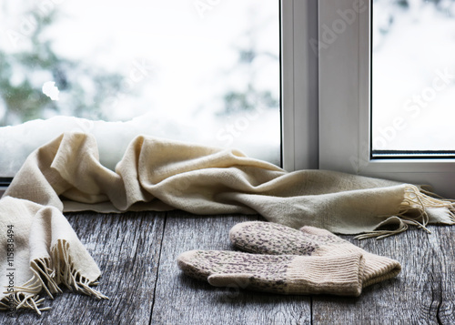 Beige woolen scarf and mittens located on wooden window sill.