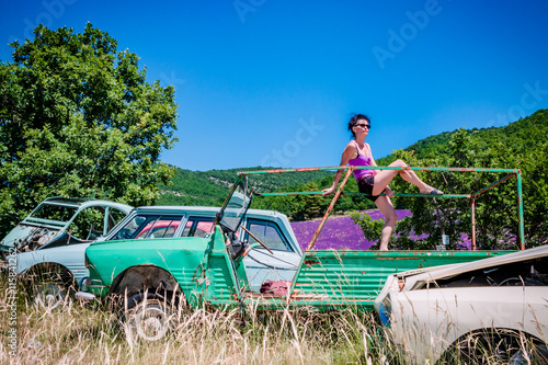 Photos Femme en short dans une casse de vieilles voitures devant les champs de lavandes