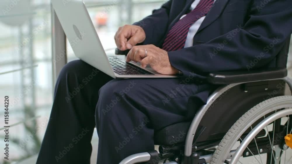 Midsection of businessman sitting in wheelchair and working on his modern laptop Midsection of businessman sitting in wheelchair and working on his modern laptop
