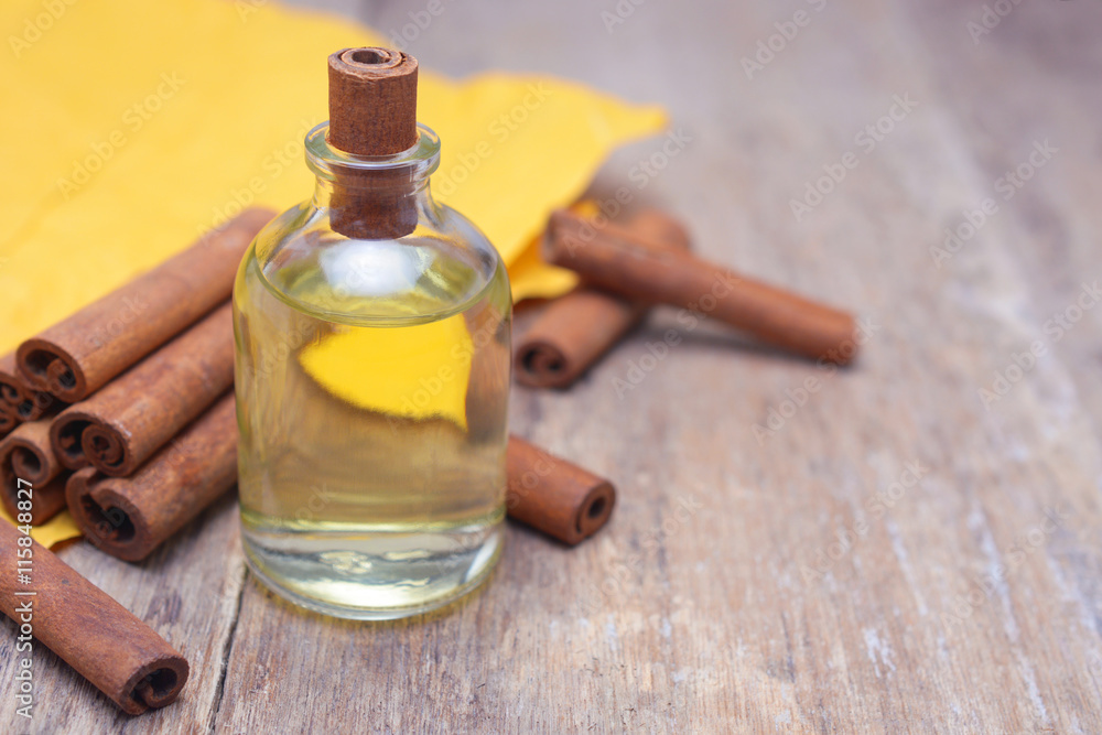 Essential aroma cinnamon oil in a glass bottle with cinnamon sticks on wooden background. Essential aroma cinnamon oil in a glass bottle with cinnamon sticks on wooden background.