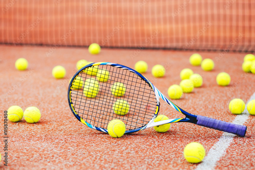 tennis racket with many balls on clay court..