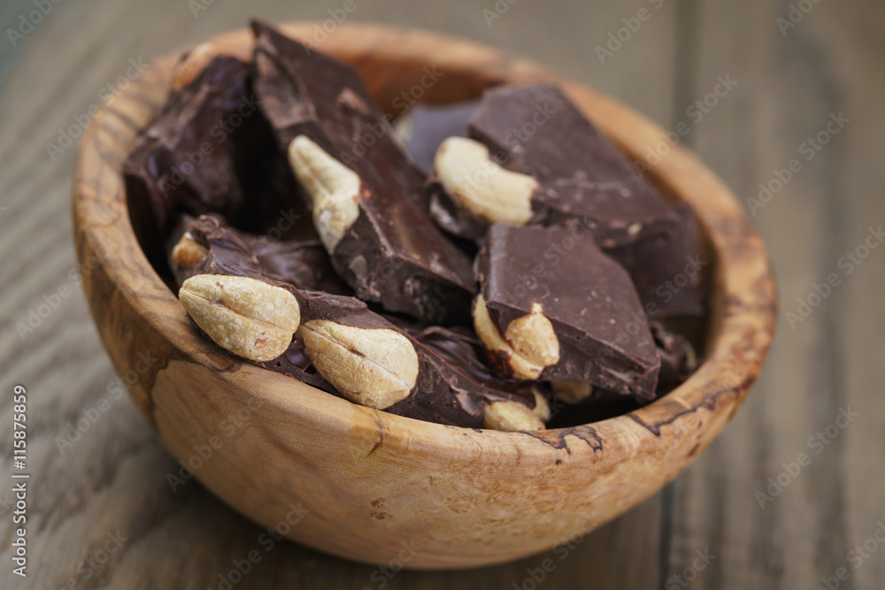 broken homemade bar of chocolate with cashew nuts in wood bowl broken homemade bar of chocolate with cashew nuts in wood bowl