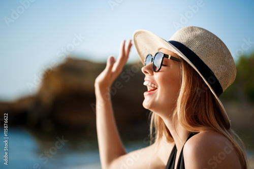 Beautiful young cheerful girl wearing glasses and hat rests at morning beach 