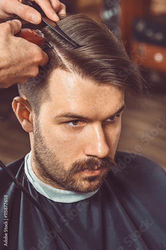 The hands of young barber making haircut to attractive man in barbershop