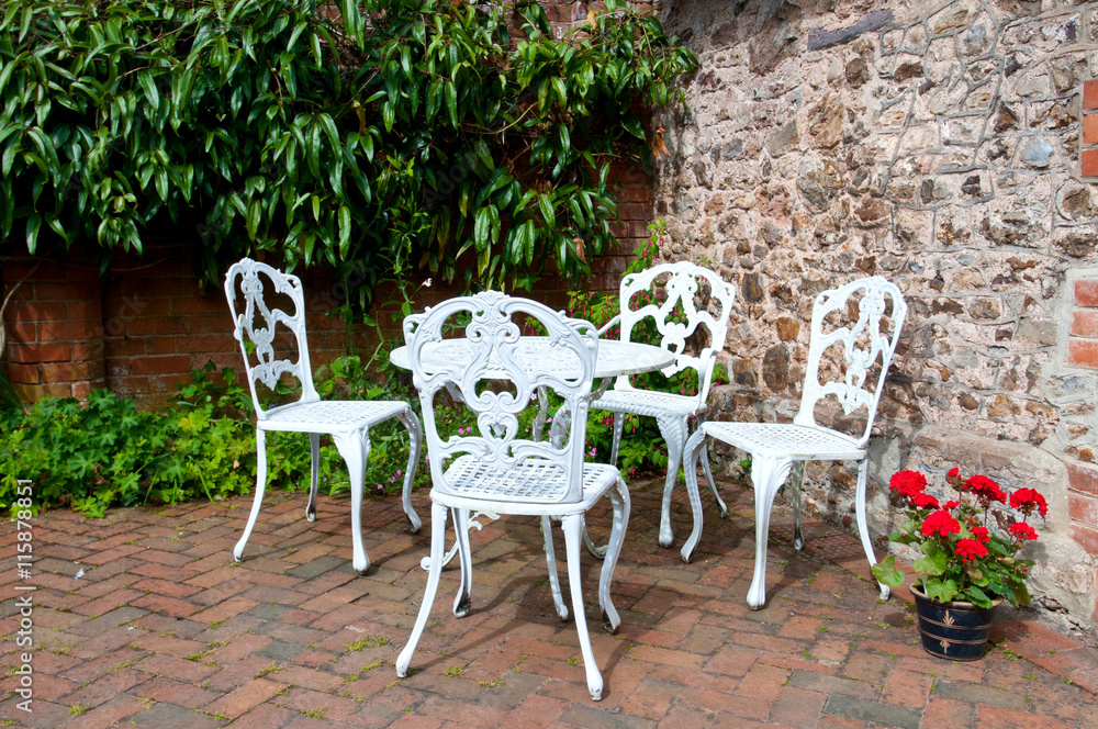 garden seating, decorative cast iron chairs and table in a courtyard garden, with pot of red pelargoniums.