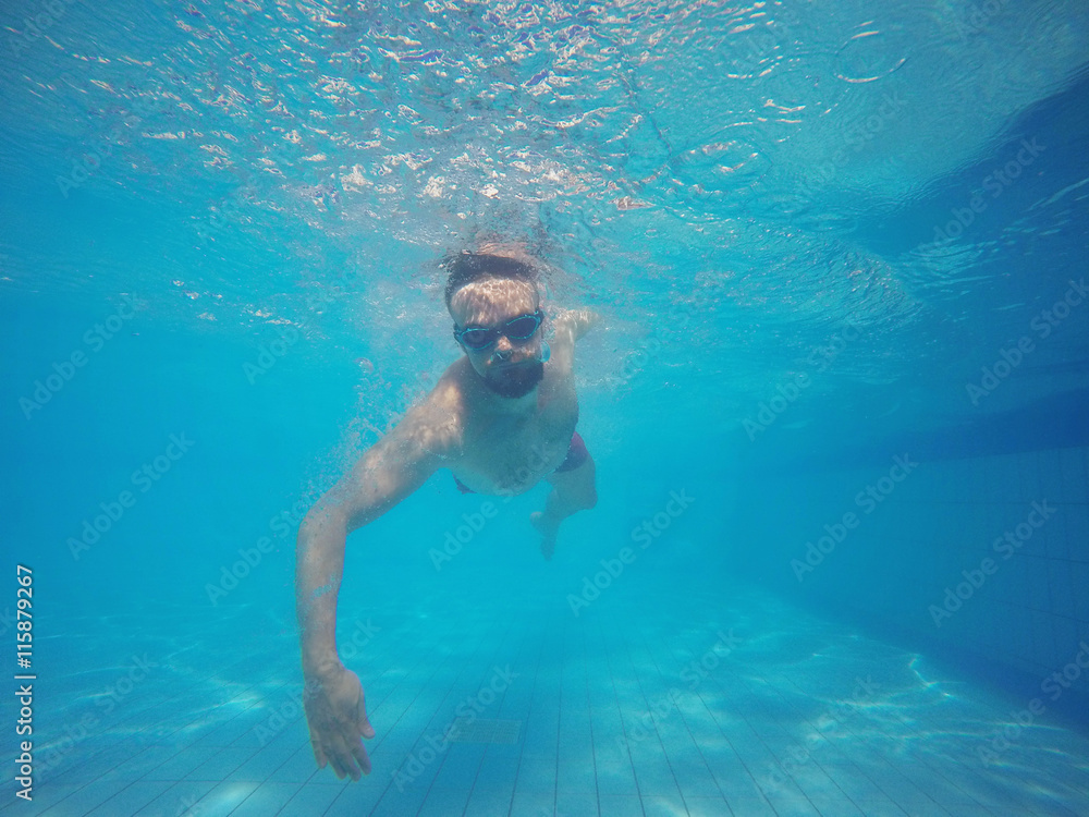 Beard man with glasses swimming under water in the pool