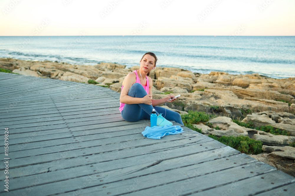 Woman resting after jogging on a wooden path at the sea