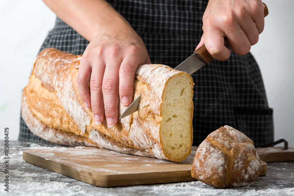 Fototapeta premium Woman cutting bread on rustic wooden table 