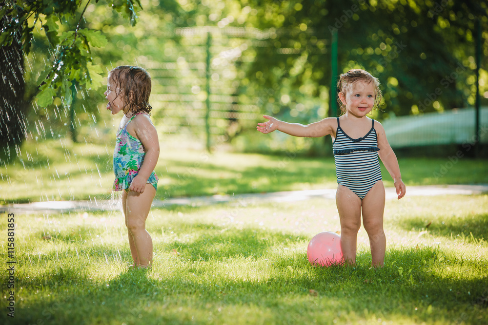 The two little baby girls playing with garden sprinkler.