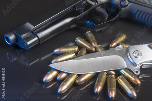 9mm hand gun with roundsand knife on black reflective background