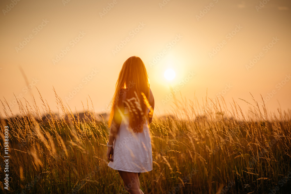 Fototapeta premium Young beautiful red-haired girl in a field at sunset