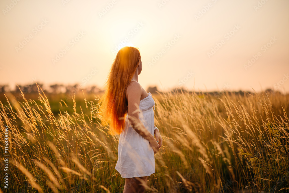 Obraz premium Young beautiful red-haired girl in a field at sunset