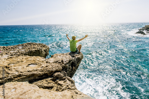 A man sits on a ledge of rock above the sea at Cape Greco . Cypr
