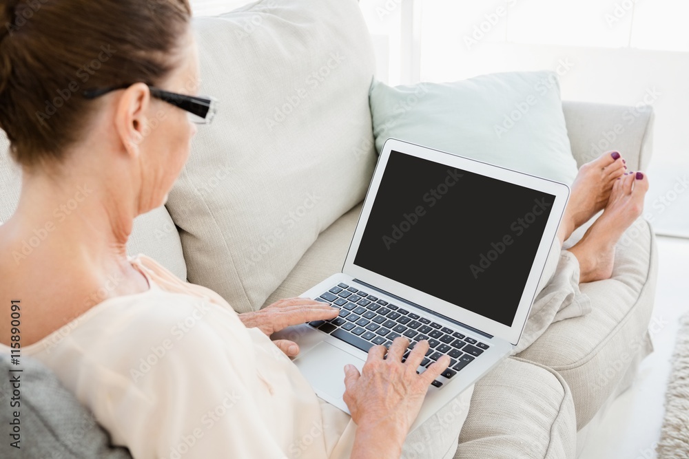 Side view of mature woman using laptop while resting on sofa Side view of mature woman using laptop while resting on sofa