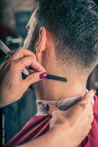 Female barber shaving a client's beard in a barber shop. Close-up
