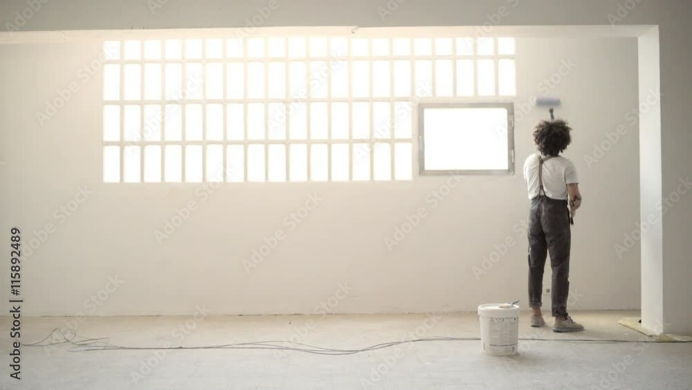 Funny curly man in pants with suspenders paints the white wall with brush roller near big industrial window and steps from one side to other Home diy renovation Loopable video. Funny curly man in pants with suspenders paints the white wall with brush roller near big industrial window and steps from one side to other Home diy renovation Loopable video.