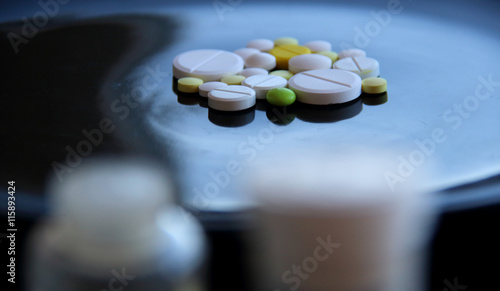 Pills bottle with soft focus over colored tablets on black surface