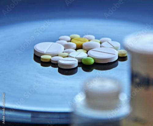 Scattered tablets on glossy surface behind plastic bottles of pills