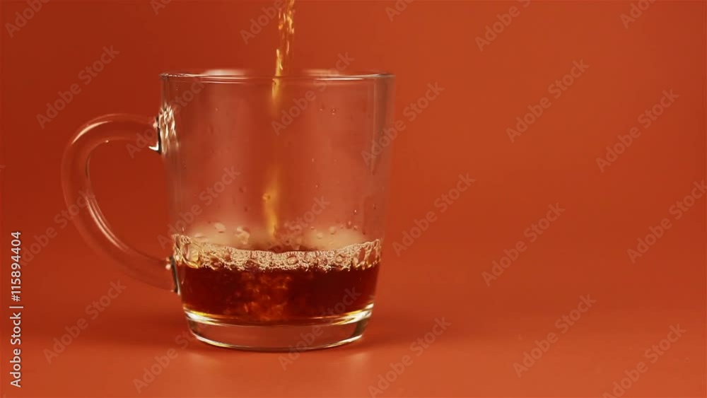 Tea being poured into glass tea cup on brown background Tea being poured into glass tea cup on brown background