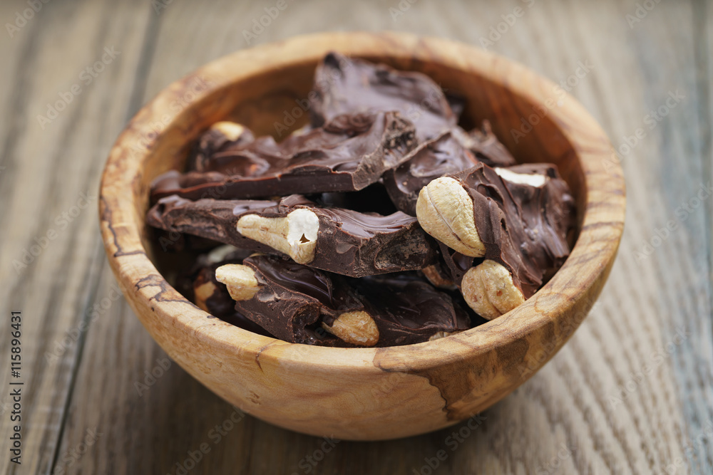 broken homemade bar of chocolate with cashew nuts in wood bowl broken homemade bar of chocolate with cashew nuts in wood bowl
