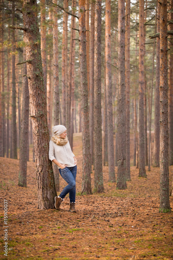 Portrait of beautiful woman standing at the old pine tree in the forest and enjoying sunlight. Girl walking in the park outdoors. Cold season. Lifestyle concept Portrait of beautiful woman standing at the old pine tree in the forest and enjoying sunlight. Girl walking in the park outdoors. Cold season. Lifestyle concept