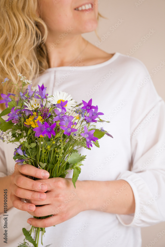 Closeup of woman's hands holding beautiful bunch of wild flowers. Girl with summer bouquet at white wall Closeup of woman's hands holding beautiful bunch of wild flowers. Girl with summer bouquet at white wall