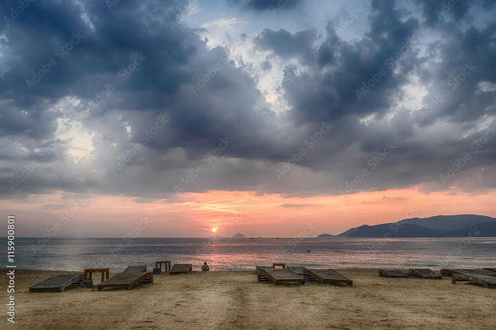 Naklejka premium Vietnam, Nha Trang, Sandy beach, empty sunbeds, the calm sea, the sunrise, a lone man is looking into the distance