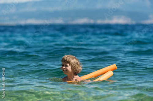 Little boy learning to swim with cell foam water noodle, water log or woggle