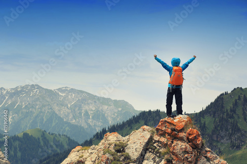 cheering successful woman backpacker open arms on mountain peak