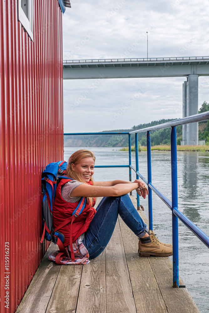 Cheerful blonde backpacker on pier smiling away Cheerful blonde backpacker on pier smiling away