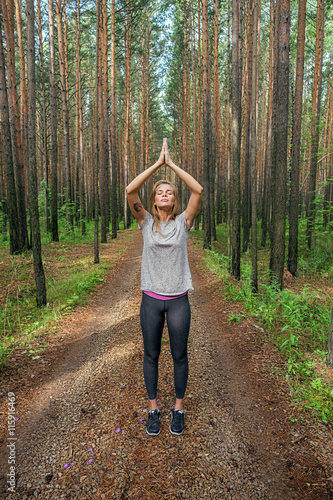 Calm meditating girl in forest with raised arms in namaste