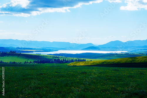 Beautiful landscape, green and yellow meadow and lake with mountain in background. Slovakia, Central Europe.