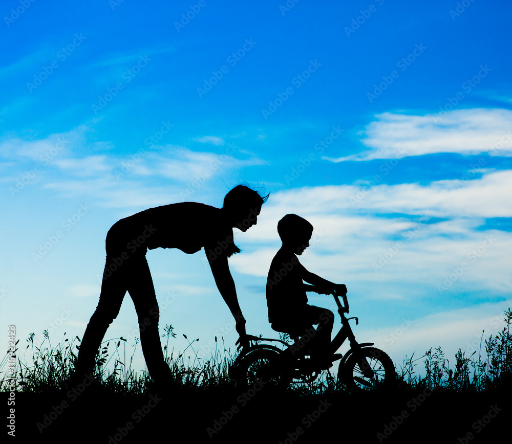 silhouette of a mother who teaches his son to ride a bike