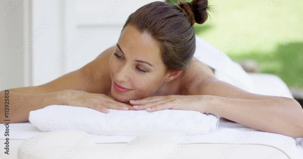 Curious woman on spa table wrapped in white towels looks to one side while resting her chin on her hands Curious woman on spa table wrapped in white towels looks to one side while resting her chin on her hands