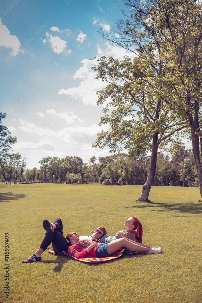 Picture of happy best friends resting and relaxing on rug in park. Summer, holidays, vacations concepts.